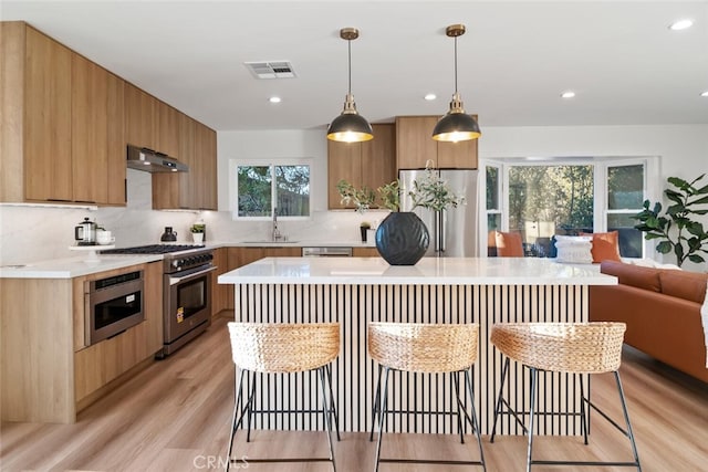 kitchen featuring appliances with stainless steel finishes, visible vents, under cabinet range hood, and a breakfast bar area