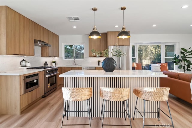 kitchen featuring visible vents, light countertops, under cabinet range hood, a kitchen bar, and premium appliances