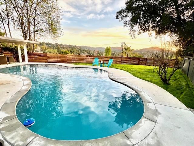 pool at dusk with a fenced in pool, a fenced backyard, a lawn, and a patio