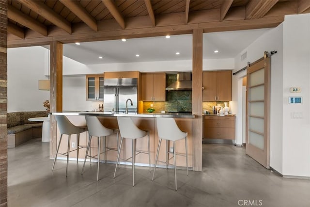 kitchen featuring a barn door, wall chimney range hood, beam ceiling, built in refrigerator, and wooden ceiling