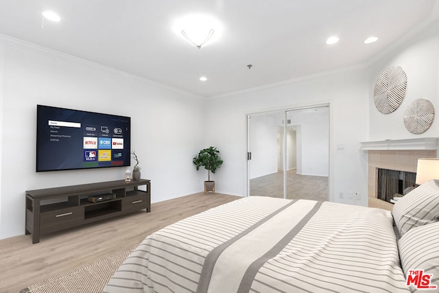 bedroom with a closet, a tile fireplace, ornamental molding, and light hardwood / wood-style flooring