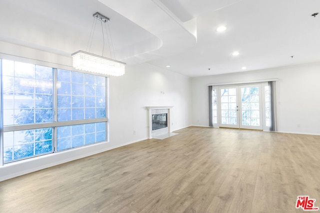 unfurnished living room featuring a fireplace, crown molding, light hardwood / wood-style flooring, french doors, and a chandelier