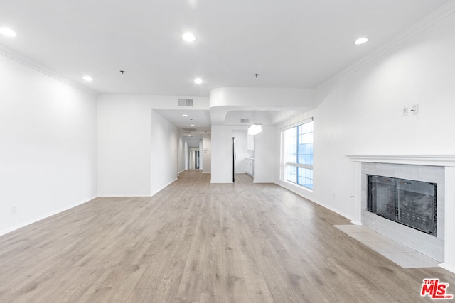 unfurnished living room with light hardwood / wood-style floors, ornamental molding, and a tiled fireplace