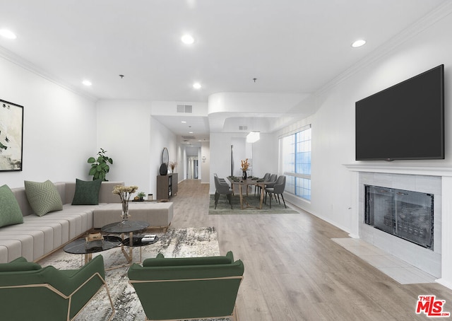 living room featuring a tile fireplace, crown molding, and light wood-type flooring