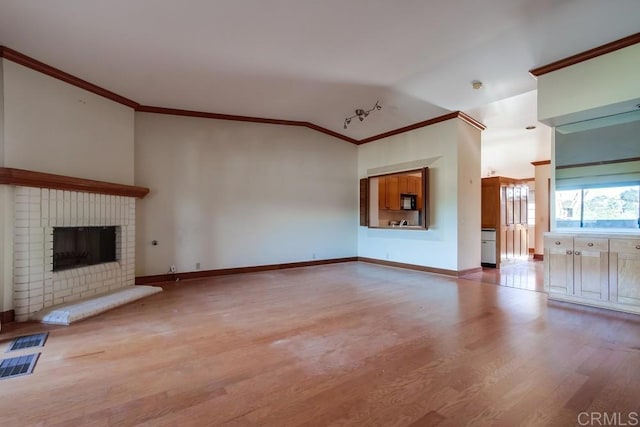 unfurnished living room with vaulted ceiling, a fireplace, ornamental molding, and light hardwood / wood-style floors