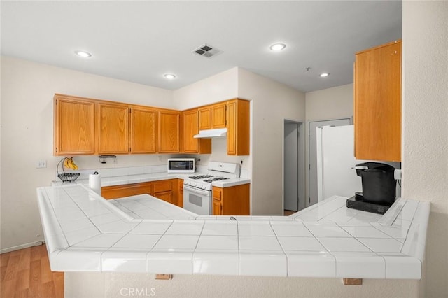 kitchen featuring kitchen peninsula, white range with gas cooktop, and tile counters