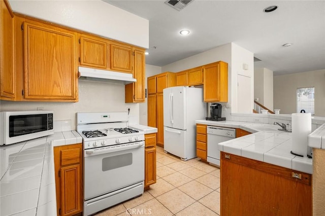 kitchen with light tile patterned floors, kitchen peninsula, tile counters, white appliances, and sink