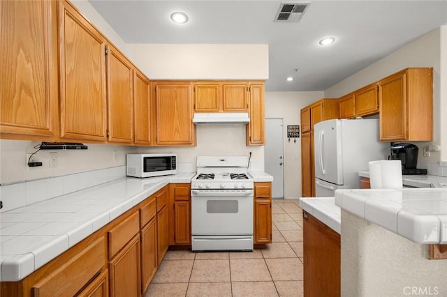 kitchen featuring light tile patterned floors, tile counters, and white appliances