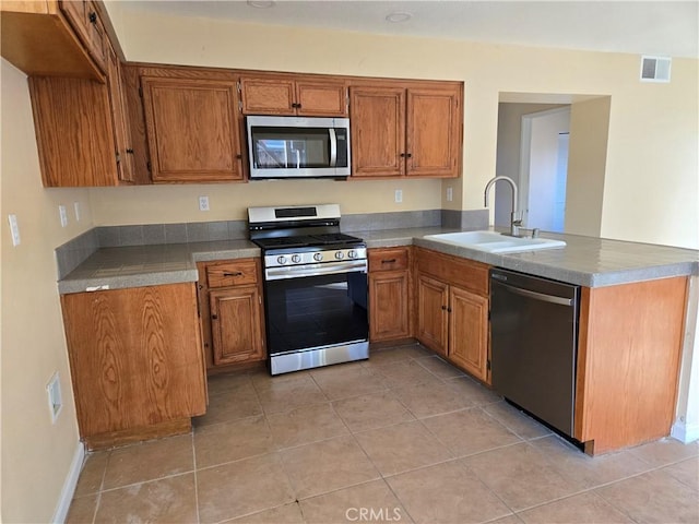 kitchen with light tile patterned floors, kitchen peninsula, appliances with stainless steel finishes, and sink