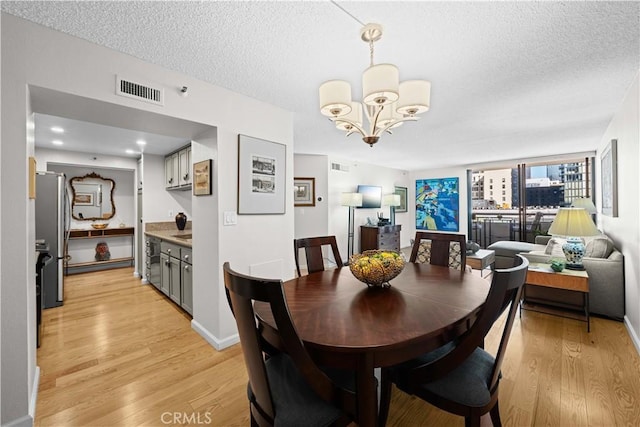 dining room featuring light wood-type flooring, a notable chandelier, and a textured ceiling