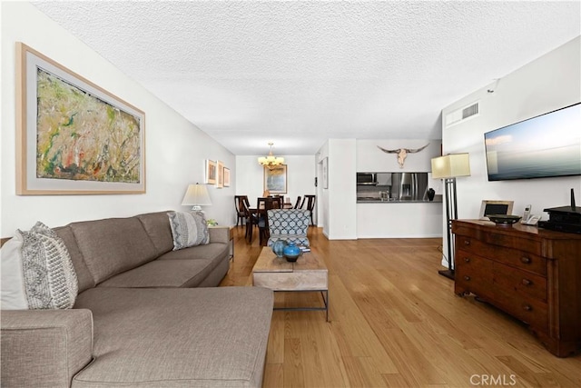 living room featuring a textured ceiling, a chandelier, and light hardwood / wood-style flooring