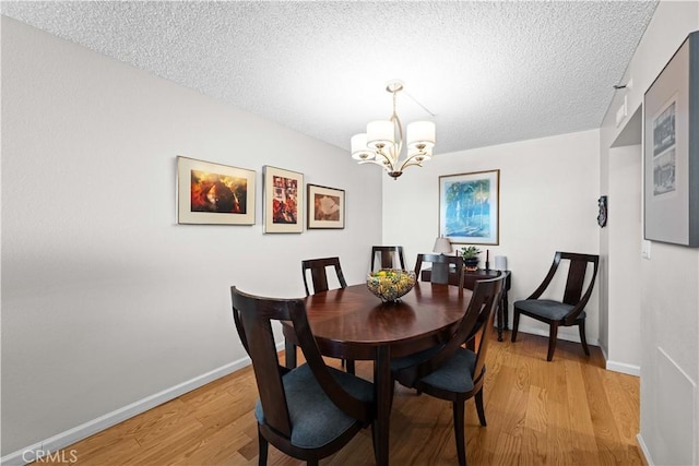 dining area with light hardwood / wood-style flooring, a chandelier, and a textured ceiling