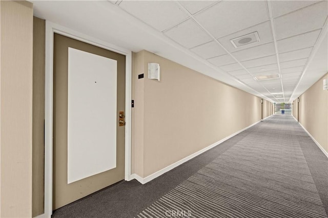 hall with a paneled ceiling and dark colored carpet