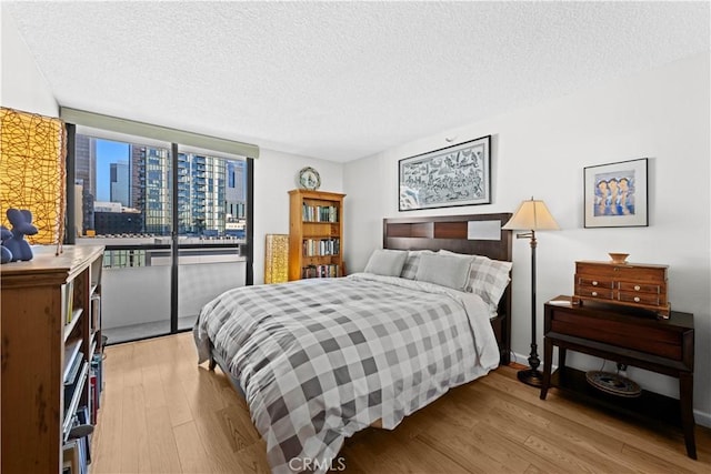 bedroom with light wood-type flooring, access to exterior, floor to ceiling windows, and a textured ceiling