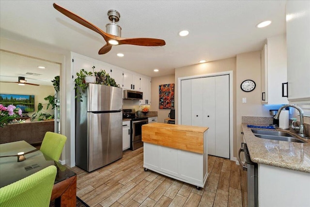 kitchen featuring light stone countertops, white cabinetry, stainless steel appliances, sink, and ceiling fan