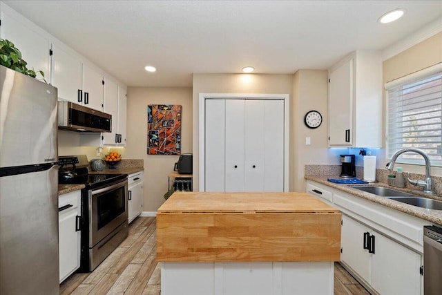 kitchen featuring butcher block counters, stainless steel appliances, a center island, white cabinets, and sink