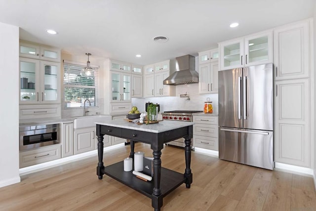 kitchen with appliances with stainless steel finishes, wall chimney exhaust hood, white cabinetry, sink, and light hardwood / wood-style flooring