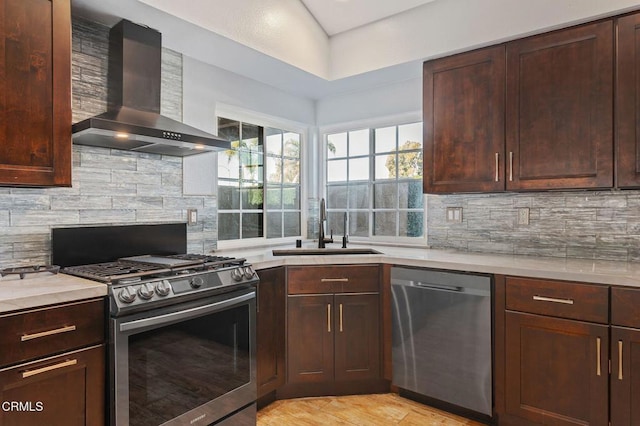 kitchen with dark brown cabinetry, appliances with stainless steel finishes, wall chimney exhaust hood, sink, and backsplash