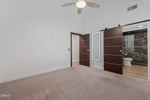 unfurnished bedroom featuring ceiling fan, a barn door, carpet floors, and ensuite bath