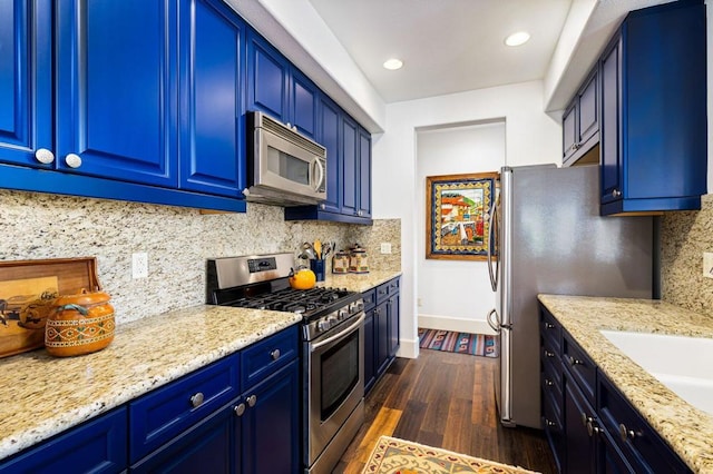 kitchen with dark wood-type flooring, appliances with stainless steel finishes, blue cabinetry, and light stone counters