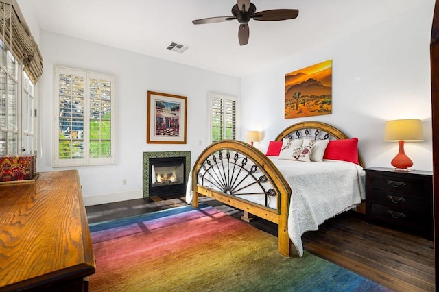 bedroom with ceiling fan, dark wood-type flooring, and a tile fireplace