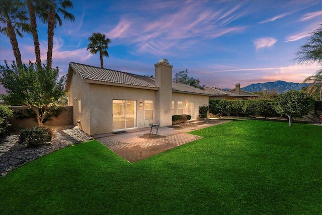 back house at dusk featuring a yard, a mountain view, and a patio