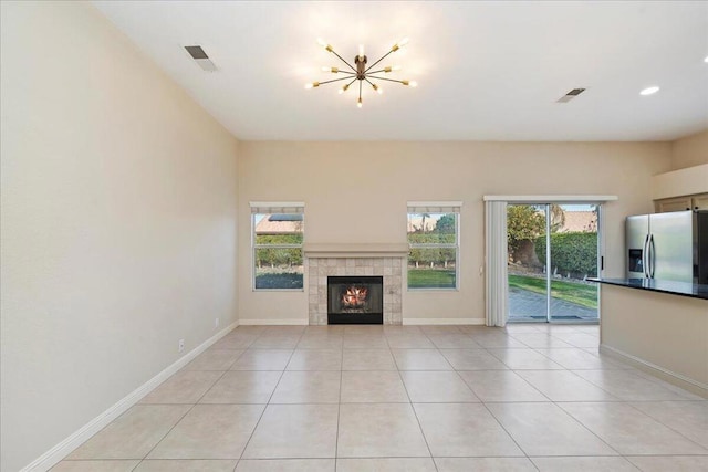 unfurnished living room with light tile patterned flooring, a tiled fireplace, and an inviting chandelier