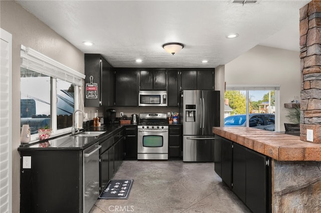 kitchen with vaulted ceiling, stainless steel appliances, a textured ceiling, and sink