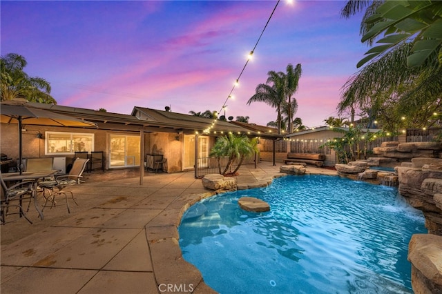 pool at dusk featuring pool water feature and a patio