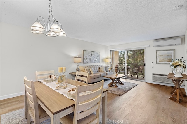 dining space featuring a textured ceiling, an inviting chandelier, light hardwood / wood-style flooring, and a wall mounted air conditioner