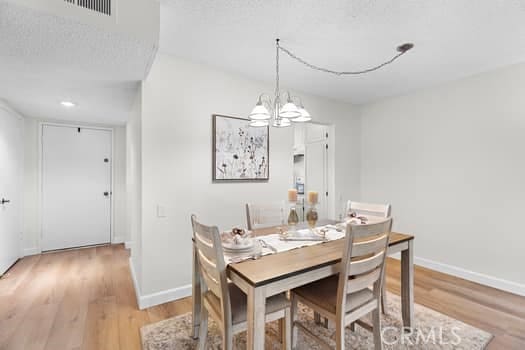 dining space with a textured ceiling, a notable chandelier, and light wood-type flooring