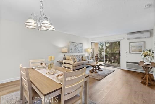 dining area featuring an inviting chandelier, wood-type flooring, and a wall mounted air conditioner