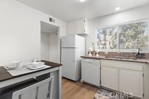 kitchen with light wood-type flooring, white cabinetry, sink, and white appliances