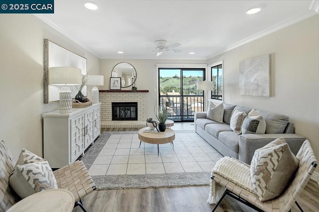 living room featuring ceiling fan, a brick fireplace, crown molding, and light hardwood / wood-style floors