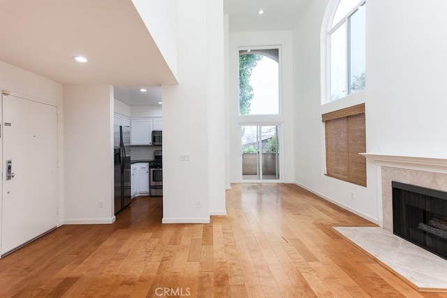 1639 Camden Ave Unit 301, Los Angeles, CA 90025 - unfurnished living room with light wood-style floors, a tile fireplace, recessed lighting, and a high ceiling
