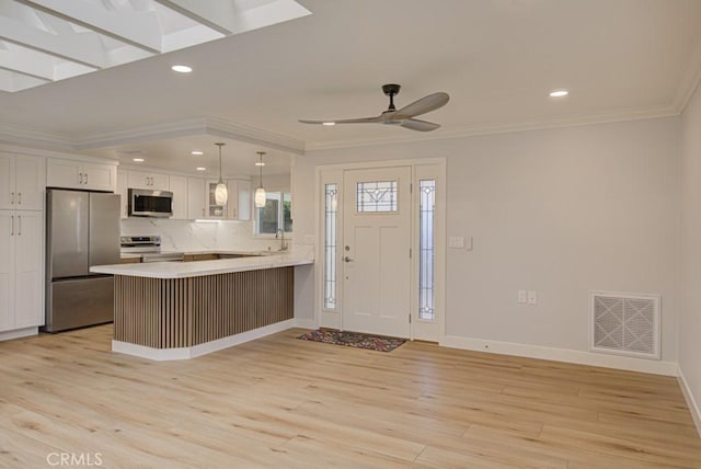 kitchen with kitchen peninsula, ceiling fan, stainless steel appliances, pendant lighting, and white cabinets