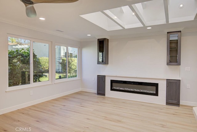 unfurnished living room with light hardwood / wood-style floors, ornamental molding, a skylight, and ceiling fan