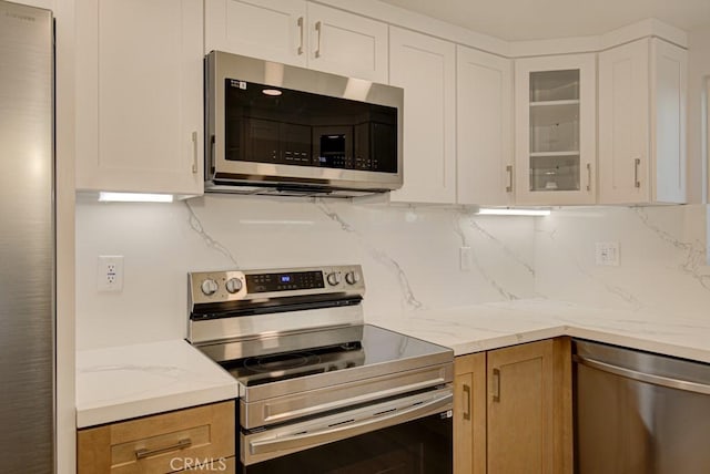 kitchen featuring white cabinets, decorative backsplash, appliances with stainless steel finishes, and light stone counters