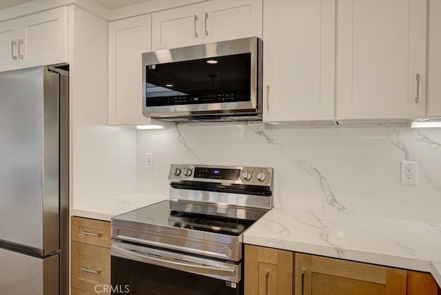 kitchen with light stone countertops, white cabinets, appliances with stainless steel finishes, and tasteful backsplash