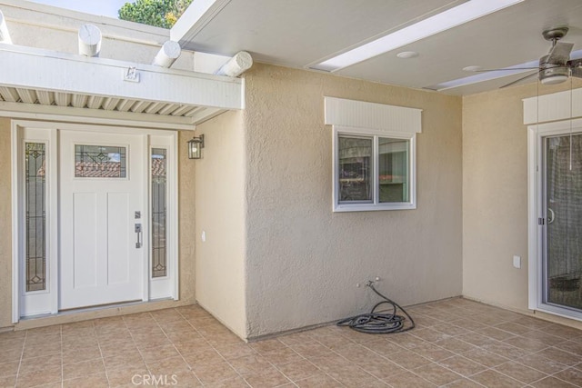 view of exterior entry with ceiling fan and a patio area