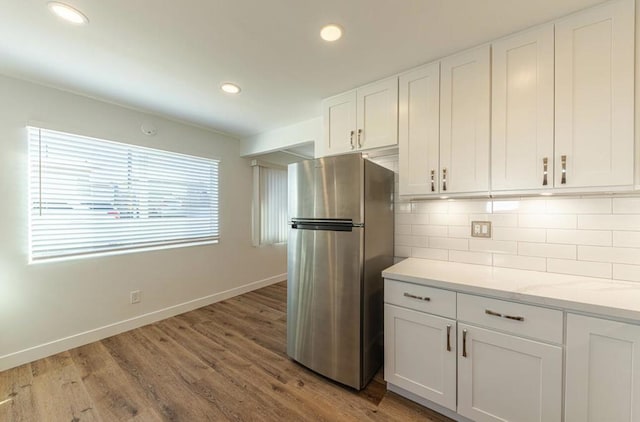 kitchen featuring light stone countertops, white cabinetry, wood-type flooring, decorative backsplash, and stainless steel fridge