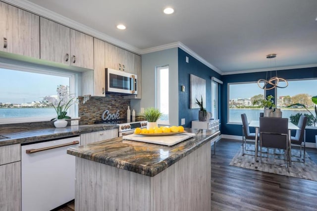 kitchen featuring appliances with stainless steel finishes, dark stone countertops, a water view, a kitchen island, and decorative light fixtures