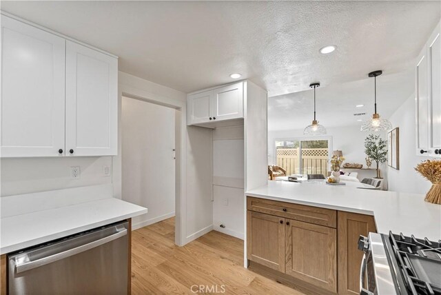 kitchen with a textured ceiling, white cabinetry, stainless steel appliances, hanging light fixtures, and light wood-type flooring