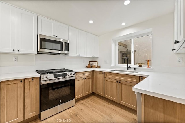 kitchen featuring sink, white cabinets, appliances with stainless steel finishes, and light wood-type flooring