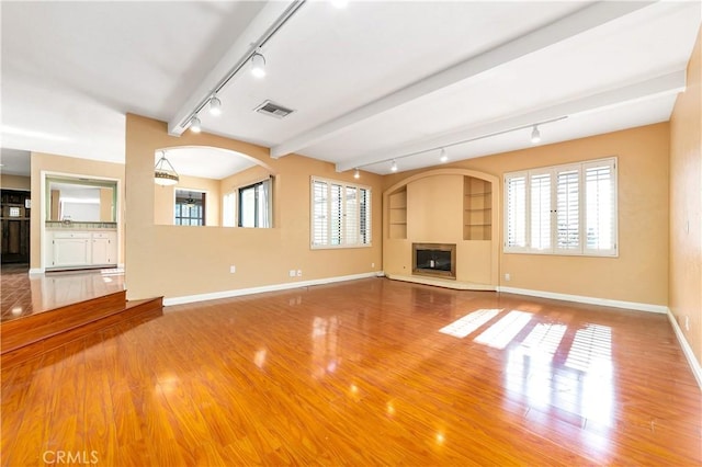 unfurnished living room featuring built in features, hardwood / wood-style flooring, a wealth of natural light, and beam ceiling