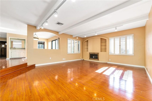 unfurnished living room with wood finished floors, visible vents, baseboards, a glass covered fireplace, and track lighting