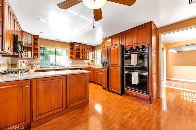 kitchen with light stone counters, stainless steel gas cooktop, open shelves, dobule oven black, and light wood-style floors