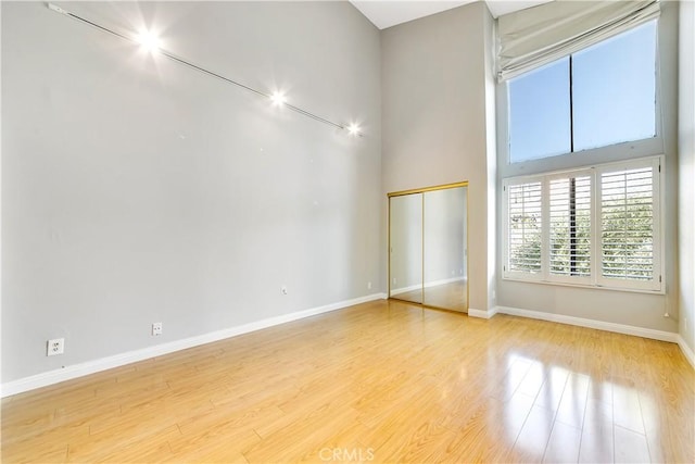 unfurnished room featuring a towering ceiling and light wood-type flooring