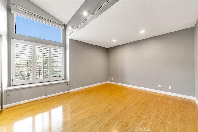 empty room featuring a textured ceiling, lofted ceiling, and light wood-type flooring