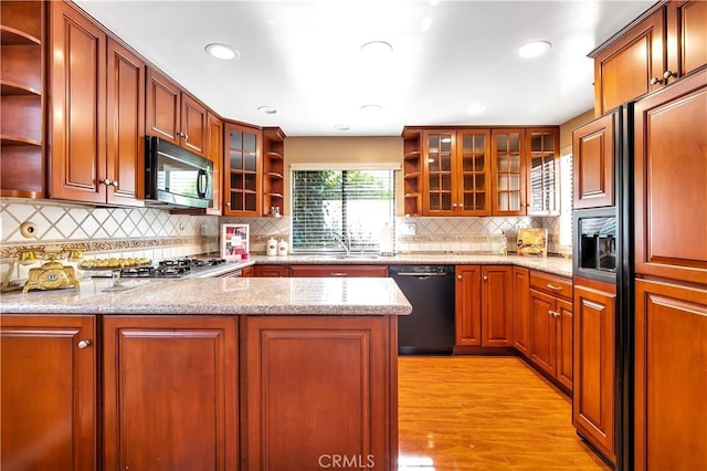 kitchen featuring kitchen peninsula, light hardwood / wood-style flooring, sink, light stone countertops, and black appliances